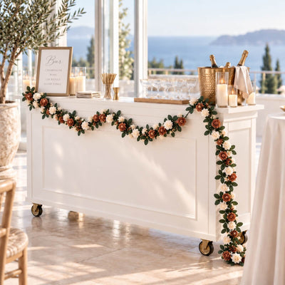 Elegant wedding bar setup with champagne, candles, and floral garland by the sea