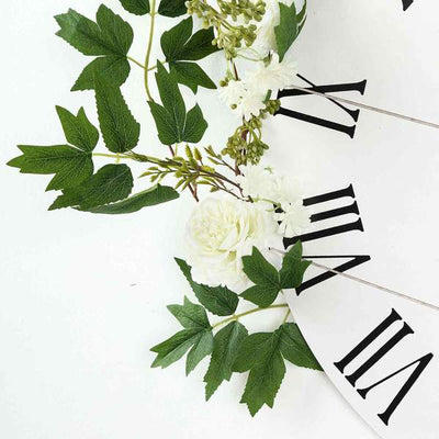 Floral wall clock with greenery and white flowers on a plain background
