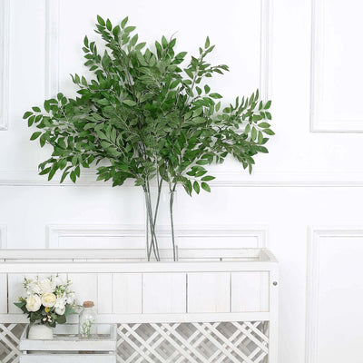 Artificial leafy branch arrangement in a decorative white vase.