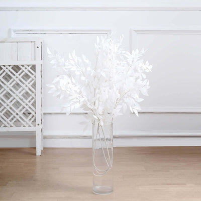 Artificial white foliage in a clear vase against a plain background.
