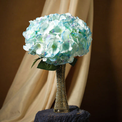 Blue hydrangea bouquet with a jeweled vase on a textured background.