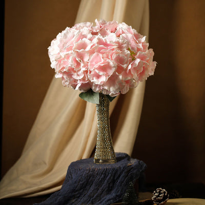 Pink hydrangea bouquet in a jeweled vase on a decorative stand.