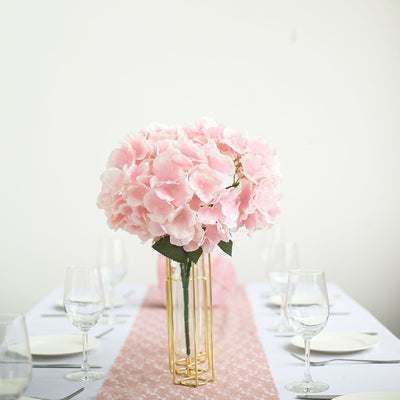 Pink hydrangea bouquet in a gold vase on a dining table setting.