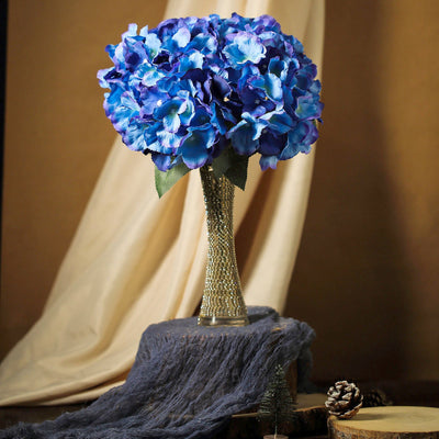 Blue hydrangea bouquet in a decorative vase on a rustic table setting.