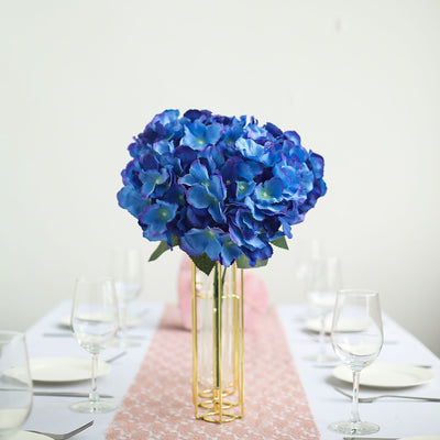 Blue artificial flower bouquet in a gold vase on a table setting.