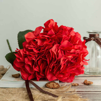 Red hydrangea flower bouquet with green leaves and brown ribbon on a rustic background.