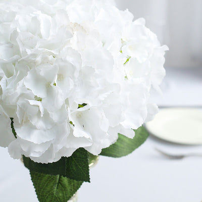 White hydrangea bouquet in a vase with green leaves on a table