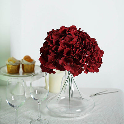 Red flower bouquet in a clear glass vase with wine glasses