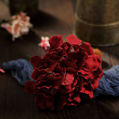 Red artificial flower bouquet on a rustic wooden surface.