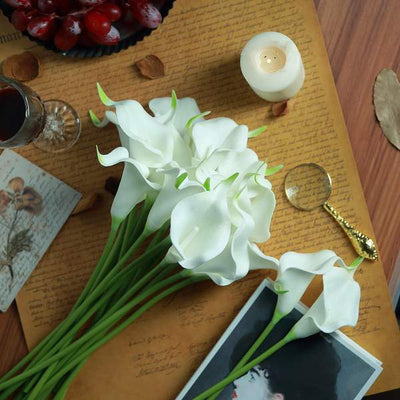 Artificial white calla lilies arranged on a wooden table with decorative items.