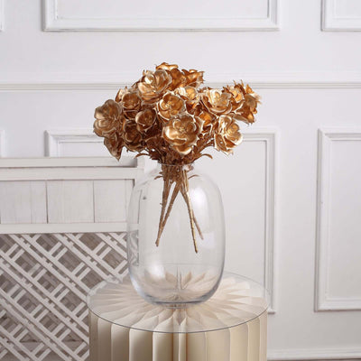 Gold artificial roses in a clear glass vase on a decorative table.