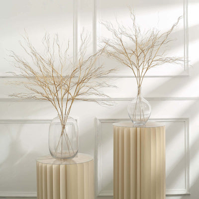 Decorative vases with dried branches on modern pedestals in a bright setting.