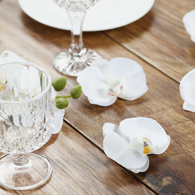 Crystal glassware with white orchid petals on a wooden table.