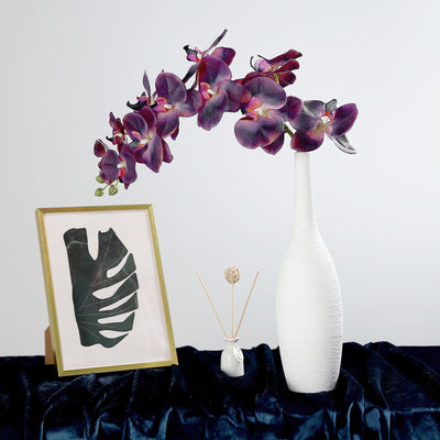Decorative vase with purple orchids and framed artwork on a dark surface.