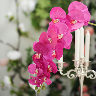 Vibrant pink orchid arrangement with candles on a decorative stand.