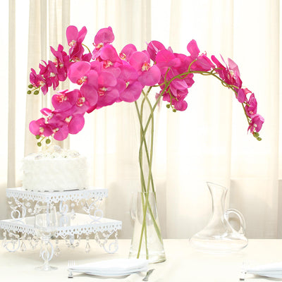 Pink orchid arrangement in a glass vase on a dining table.