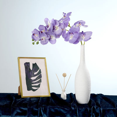 Orchid flower arrangement in a white vase with decorative elements on a table.