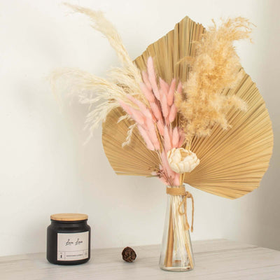 Dried flower arrangement in a glass vase with a candle beside it.