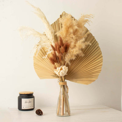 Dried flower arrangement in a glass vase with a candle, styled on a table.