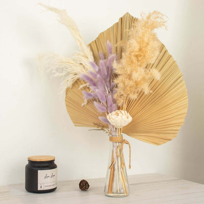 Dried flower arrangement in a glass vase with a candle on a table.