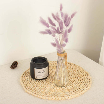 Black candle and dried flowers in a vase on a woven placemat.