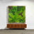 Artificial green wall art in a wooden frame above a modern sideboard.