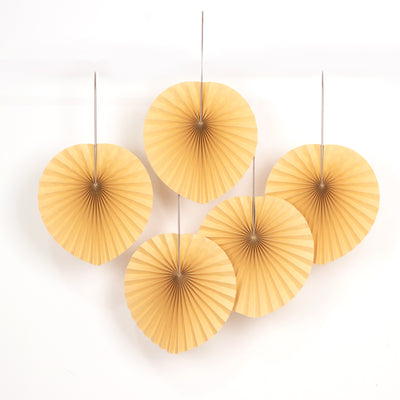 Five decorative paper fans in warm yellow tones hanging on a white backdrop.