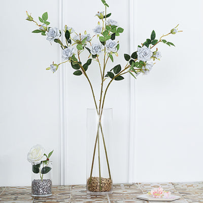 Artificial white rose arrangement in a clear vase with decorative stones.