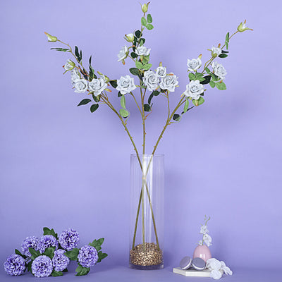 Elegant faux flowers in a clear vase with decorative stones and soft pastel backdrop.