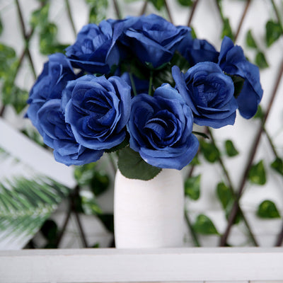 Blue artificial roses in a white vase against a green backdrop.