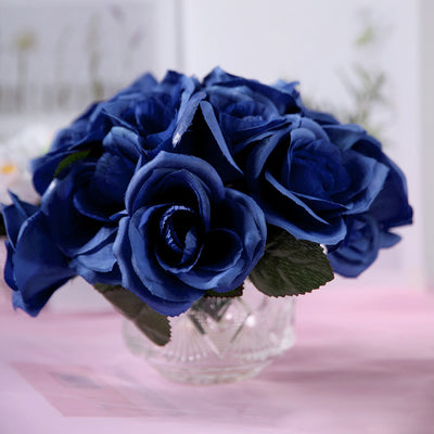 Blue rose bouquet in a crystal vase with green leaves.