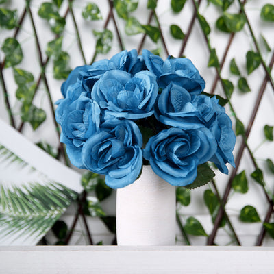 Blue rose bouquet in a white vase against a green backdrop.