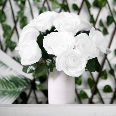 White artificial roses in a vase against a green backdrop.