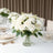 Elegant white floral arrangement in a glass vase on a dining table.