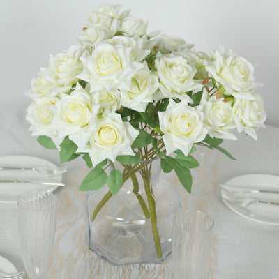 White artificial roses in a clear vase on a dining table.