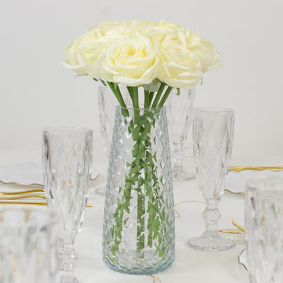 White roses in a clear vase on a dining table with crystal glassware.