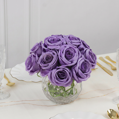 Purple rose bouquet in a clear vase on a dining table.