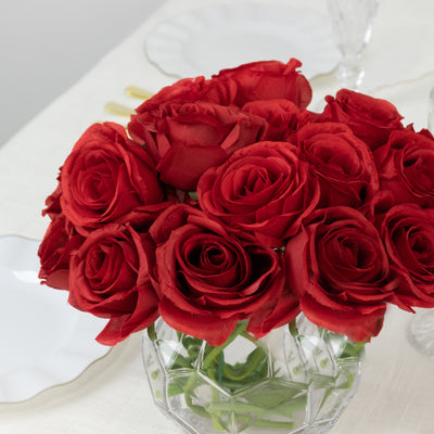 Red roses bouquet in a clear vase on a dining table.
