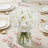 White rose bouquet in a glass vase on a dining table setting.