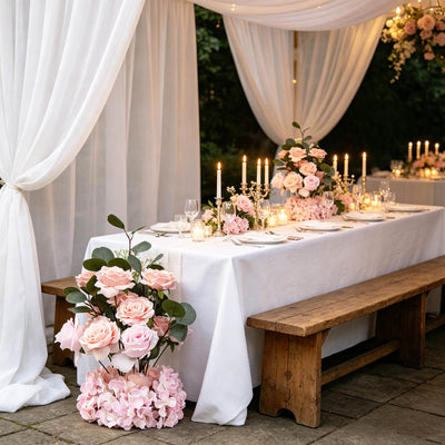 Elegant outdoor wedding table with pink roses, candles, and white drapery