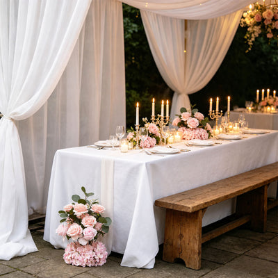 Elegant outdoor wedding table with pink roses, candles, and white drapery
