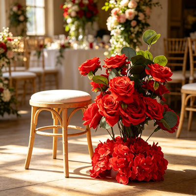 Red rose floral arrangement beside a wooden stool in a sunlit wedding venue