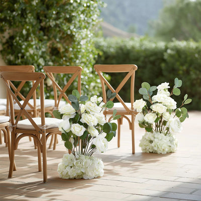 White floral arrangements beside wooden chairs for outdoor event decor.