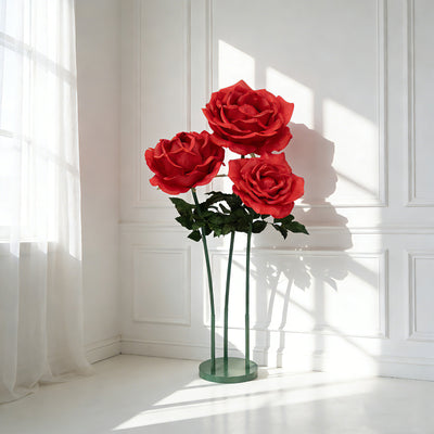 Large red roses in a modern vase, casting shadows on a white wall.