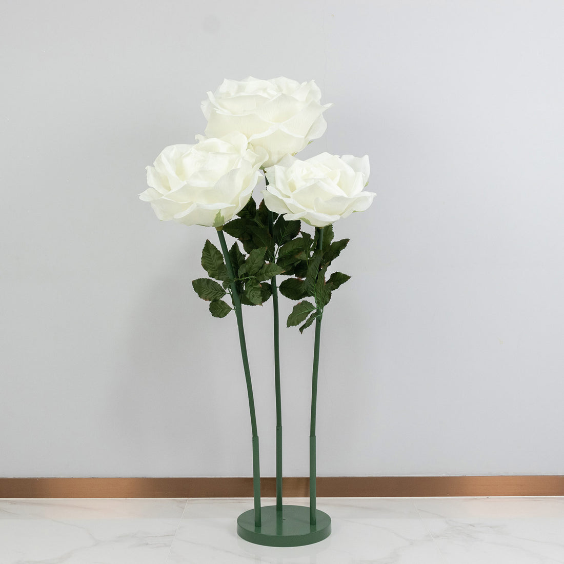 White roses in a green stand against a plain wall backdrop