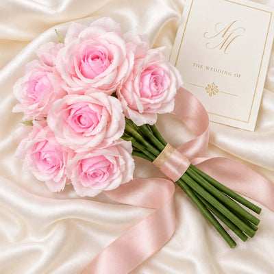 Pink rose bridal bouquet with wedding invitation on satin backdrop