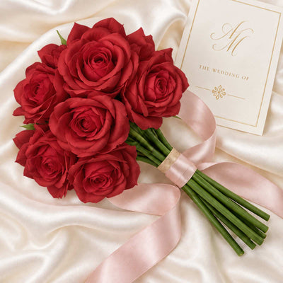 Red rose bridal bouquet with wedding invitation on satin backdrop