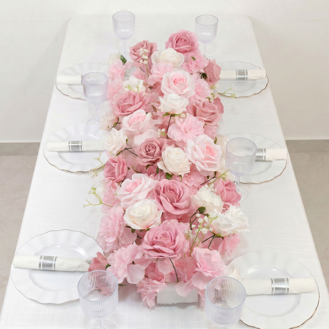 Pink floral table centerpiece with white plates, napkins, and glassware
