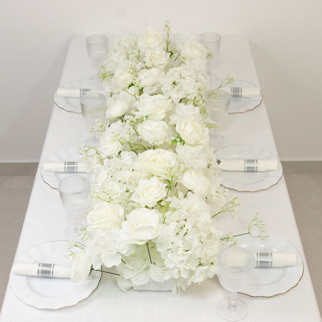 White floral centerpiece on a dining table with elegant glassware and plates.