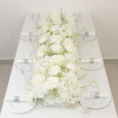 White floral centerpiece on a dining table with elegant glassware and plates.